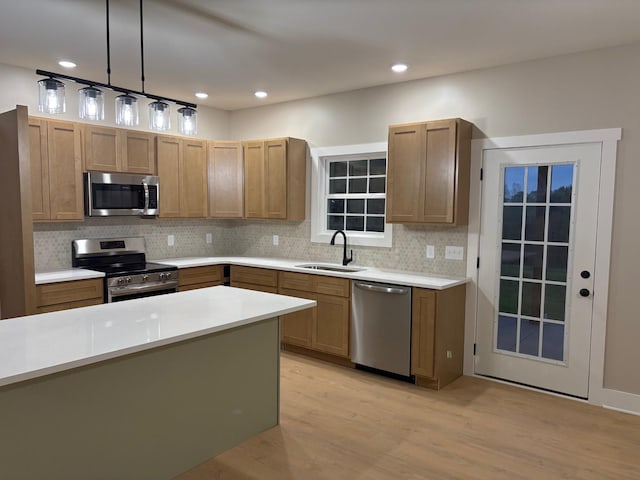 kitchen with appliances with stainless steel finishes, tasteful backsplash, a sink, light countertops, and light wood-style flooring