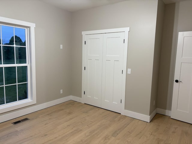 unfurnished bedroom with a closet, baseboards, visible vents, and light wood-type flooring