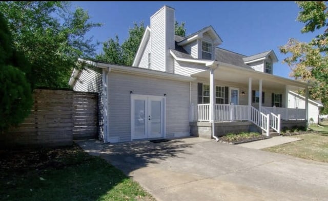 view of front facade with french doors, covered porch, and a chimney
