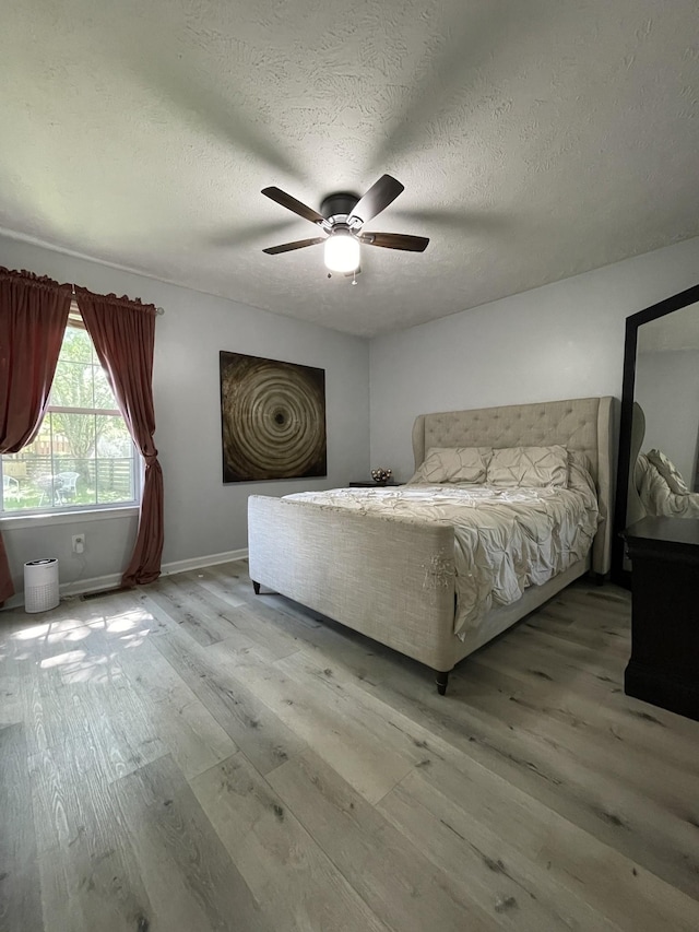 bedroom featuring baseboards, a ceiling fan, a textured ceiling, and light wood-style flooring