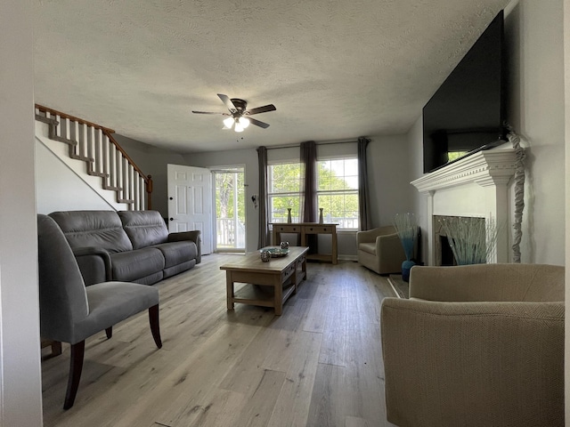 living area featuring stairs, light wood-style floors, ceiling fan, a textured ceiling, and a premium fireplace