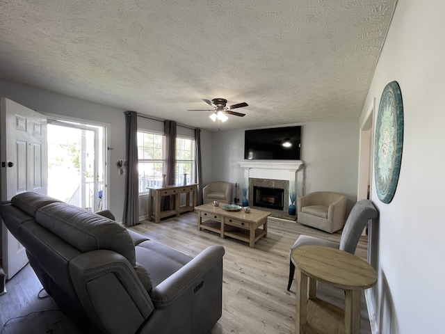 living area featuring a textured ceiling, light wood-style flooring, a ceiling fan, and a fireplace