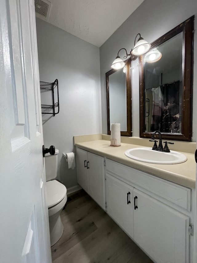 bathroom featuring visible vents, vanity, wood finished floors, toilet, and a shower with shower curtain