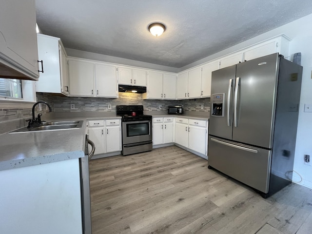 kitchen featuring appliances with stainless steel finishes, a sink, light wood-style floors, backsplash, and under cabinet range hood