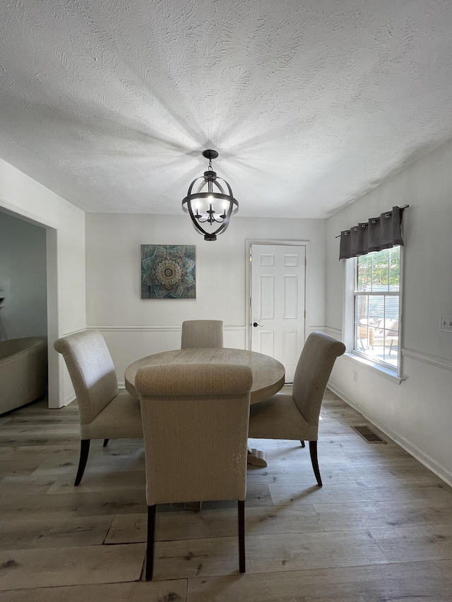 dining area with visible vents, a textured ceiling, wood finished floors, and a notable chandelier