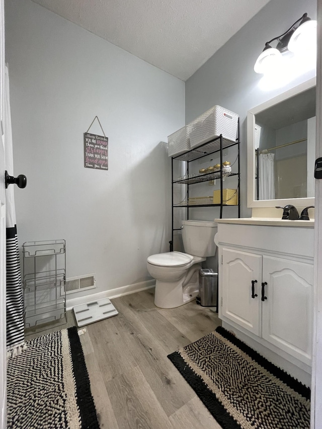 bathroom featuring a textured ceiling, wood finished floors, vanity, baseboards, and toilet