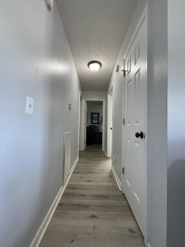 corridor with baseboards, a textured ceiling, visible vents, and wood finished floors