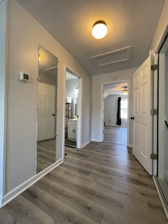corridor with baseboards, attic access, a textured ceiling, and wood finished floors