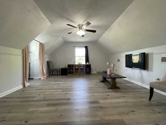 bonus room featuring wood finished floors, lofted ceiling, baseboards, ceiling fan, and a textured ceiling
