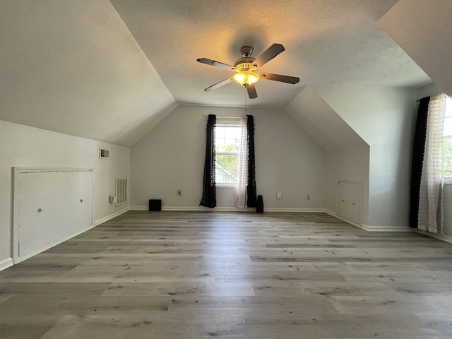 bonus room featuring a textured ceiling, a ceiling fan, lofted ceiling, light wood-type flooring, and visible vents