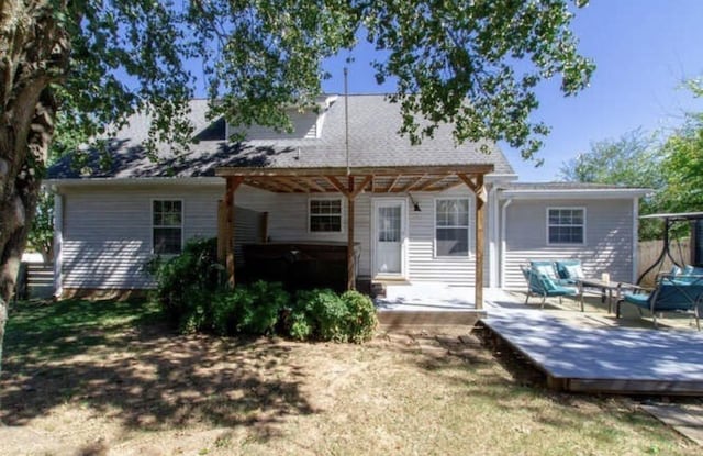 rear view of house featuring a wooden deck, a hot tub, and a pergola