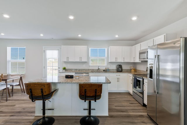 3008 Sapgate Ln, Nashville, TN 37207 - kitchen with a kitchen island, a kitchen bar, appliances with stainless steel finishes, white cabinets, and dark wood-type flooring