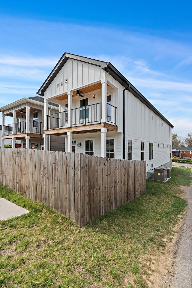 exterior space featuring fence, central AC, a ceiling fan, board and batten siding, and a lawn