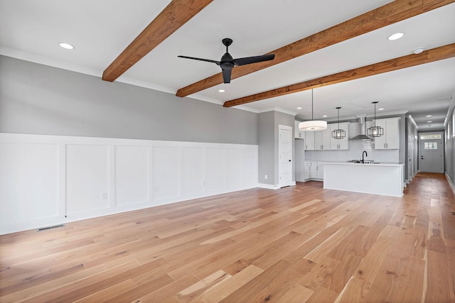 unfurnished living room with light wood-style flooring, a sink, beamed ceiling, and visible vents
