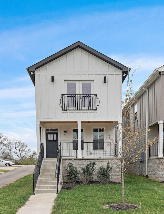 view of front of property featuring a balcony, covered porch, board and batten siding, and a front yard