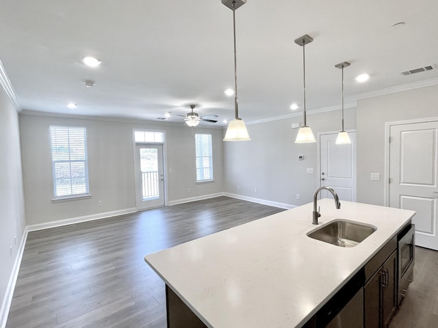 kitchen with a center island with sink, dark wood-style floors, crown molding, and a sink