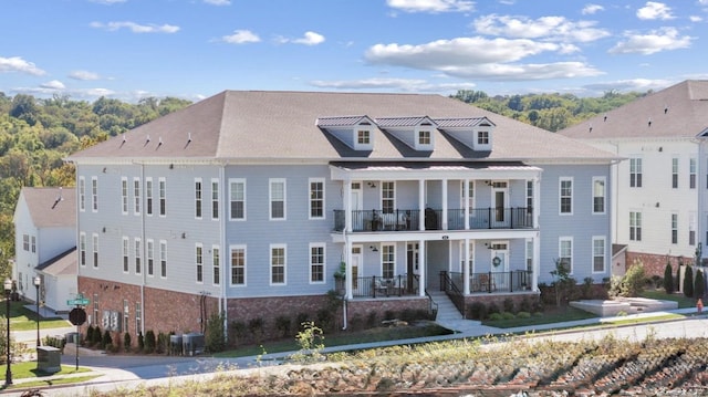 view of front of house with a balcony, brick siding, a porch, and central AC unit