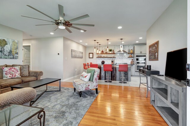 living room with a ceiling fan, bar, light wood-style flooring, baseboards, and recessed lighting
