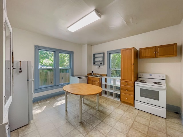 kitchen featuring baseboards, plenty of natural light, brown cabinetry, and white appliances