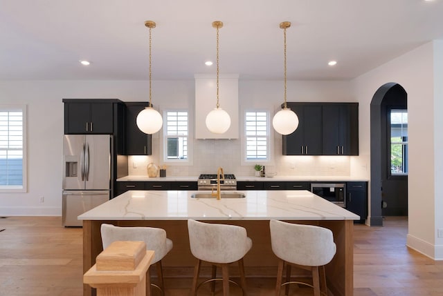 kitchen featuring arched walkways, a sink, appliances with stainless steel finishes, dark cabinets, and backsplash