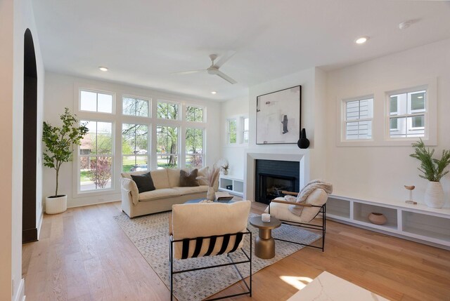living area featuring light wood-style floors, plenty of natural light, a fireplace, and ceiling fan