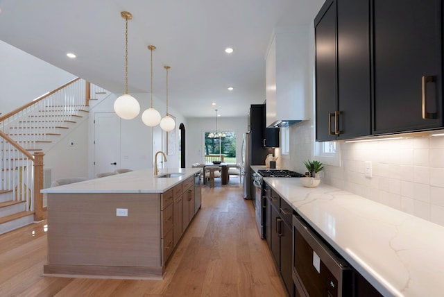 kitchen featuring a sink, appliances with stainless steel finishes, dark cabinetry, light wood-style floors, and backsplash