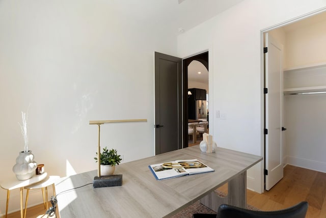 home office with arched walkways, baseboards, and wood finished floors