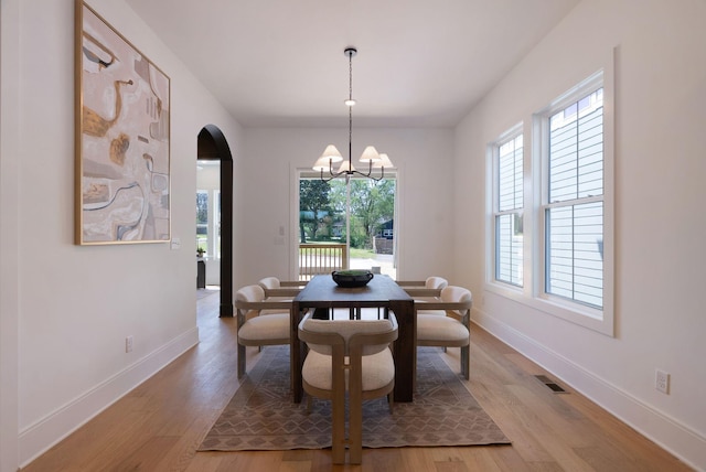 dining space featuring visible vents, light wood finished floors, arched walkways, and a chandelier