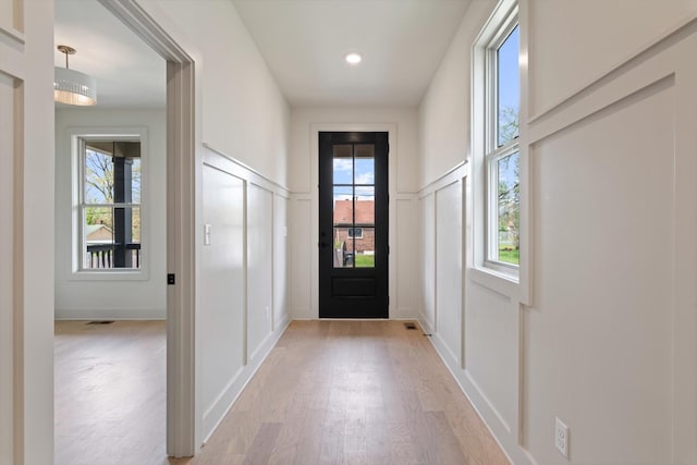 doorway to outside featuring wainscoting, light wood-style flooring, and a decorative wall