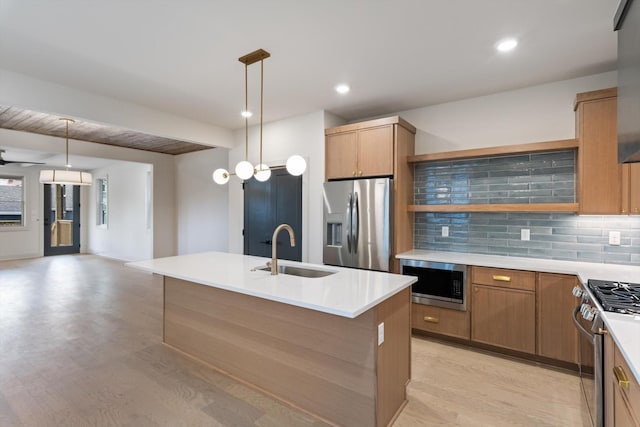 kitchen with stainless steel appliances, open shelves, a sink, light wood-style floors, and a center island with sink