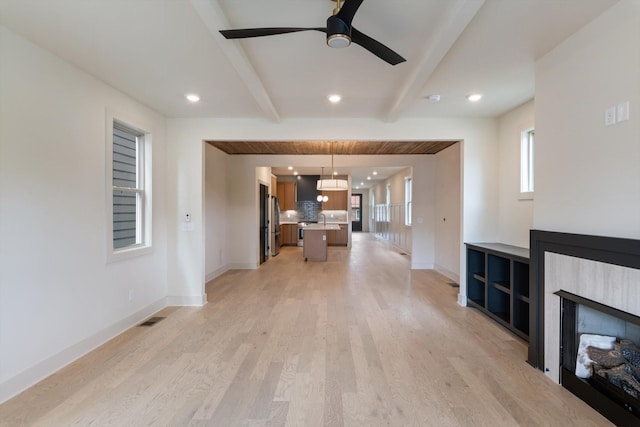 unfurnished living room featuring ceiling fan, baseboards, light wood finished floors, and beamed ceiling