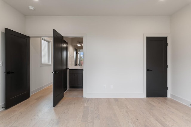 unfurnished bedroom featuring light wood-style flooring, baseboards, and ensuite bathroom