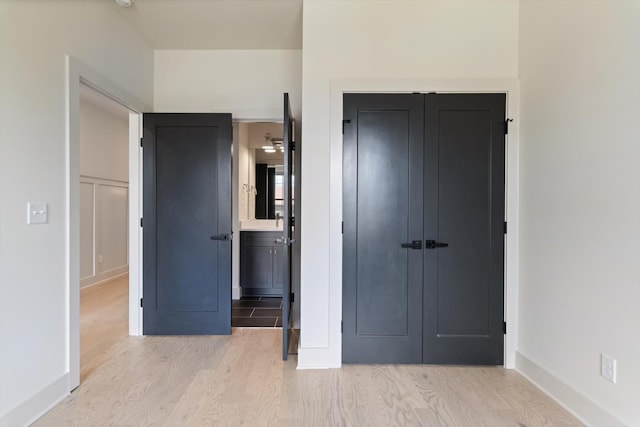 unfurnished bedroom with connected bathroom, baseboards, light wood-style flooring, and a closet
