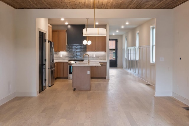 kitchen with light wood-type flooring, an island with sink, appliances with stainless steel finishes, and wall chimney range hood