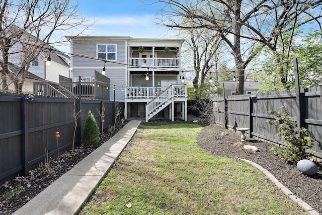 back of house featuring stairs, a fenced backyard, a balcony, a lawn, and ceiling fan