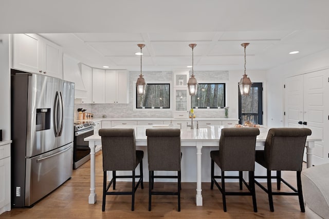 kitchen featuring white cabinets, a breakfast bar, stainless steel appliances, light wood-style floors, and coffered ceiling