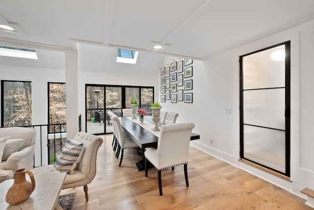 dining room featuring a skylight, baseboards, and light wood finished floors
