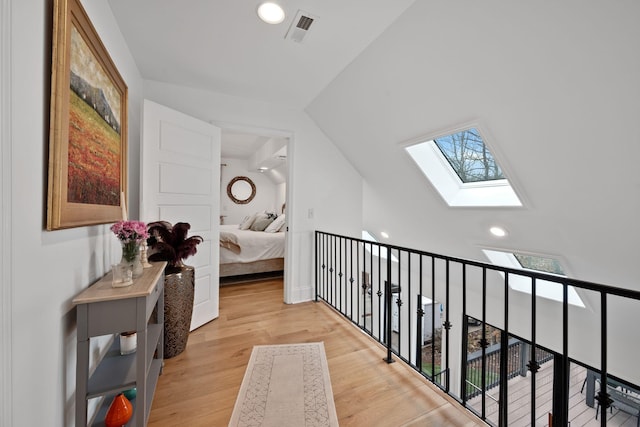 hall featuring a wealth of natural light, visible vents, vaulted ceiling with skylight, and wood finished floors