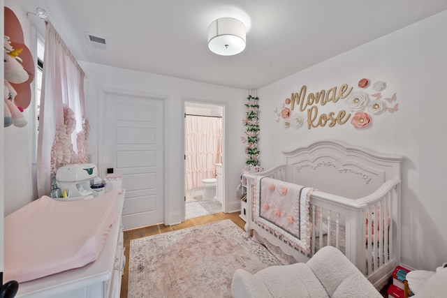 bedroom featuring connected bathroom, visible vents, a nursery area, and light wood finished floors