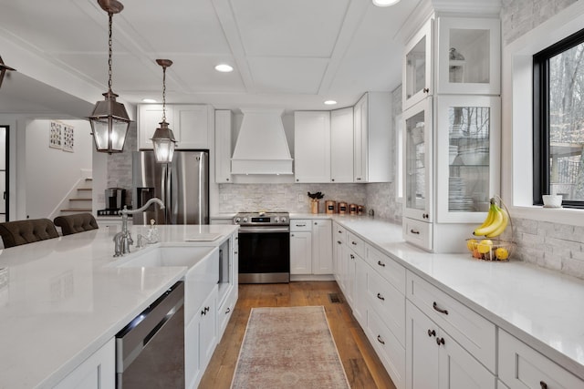 kitchen featuring white cabinetry, light wood-type flooring, custom range hood, stainless steel appliances, and hanging light fixtures