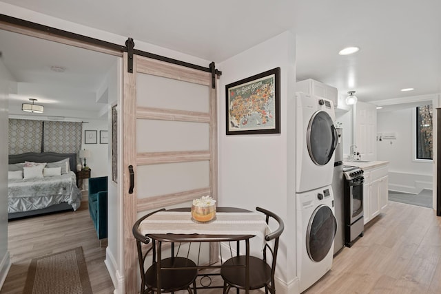 clothes washing area with light wood-type flooring, a barn door, stacked washer / dryer, and laundry area
