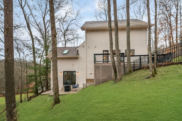 rear view of property featuring a lawn, roof with shingles, a deck, and a patio area