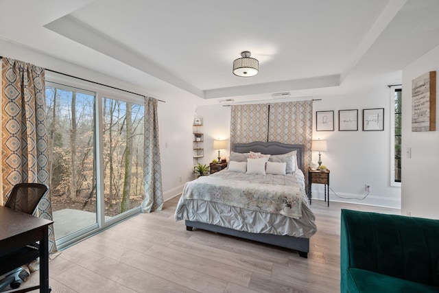 bedroom with visible vents, a tray ceiling, baseboards, and wood finished floors