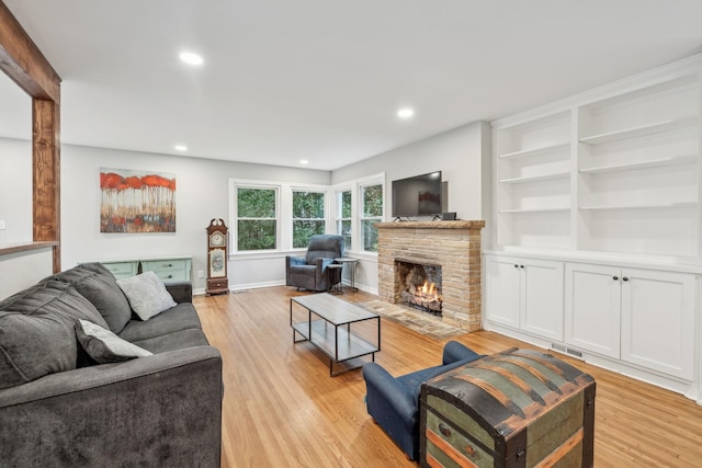 living area featuring visible vents, light wood-style flooring, a fireplace, recessed lighting, and built in features