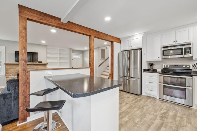 kitchen featuring white cabinets, beamed ceiling, light wood finished floors, stainless steel appliances, and dark countertops