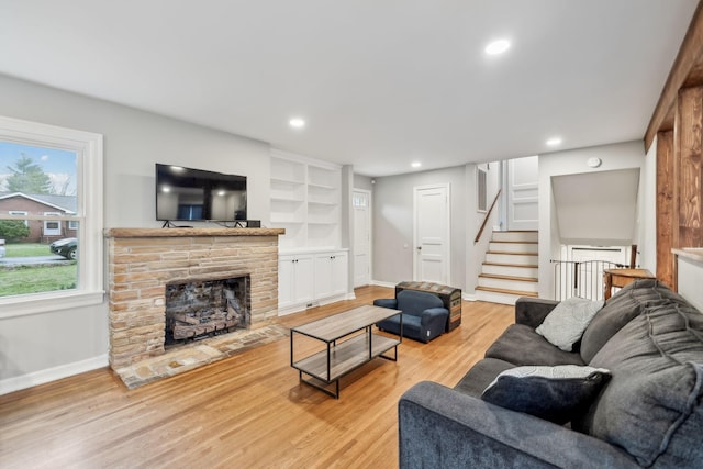 living room with stairs, recessed lighting, baseboards, light wood-style floors, and a stone fireplace