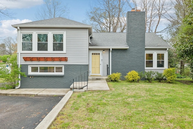view of front of home with a chimney, a front yard, brick siding, and roof with shingles