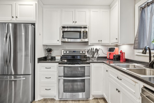 kitchen featuring white cabinetry, dark countertops, a sink, and stainless steel appliances