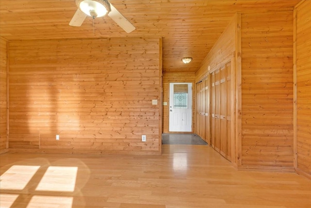 spare room featuring wooden walls, wood finished floors, wood ceiling, and a ceiling fan