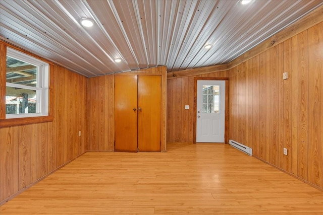 unfurnished room featuring plenty of natural light, wood walls, light wood-style floors, and a baseboard heating unit